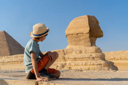 The boy in hat sits in front of the sphinx and looks at itの写真素材
