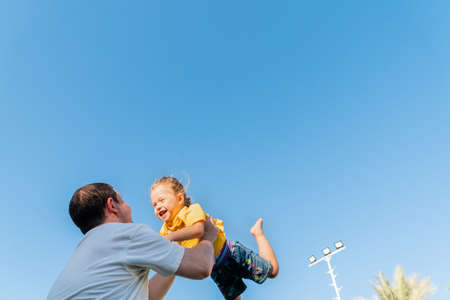 Happy father throwing up baby against blue skyの写真素材