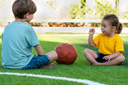Cute little girl sitting on lawn with brother and talking with him