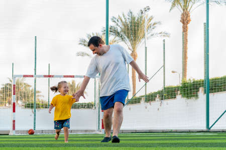 Happy father and daughter running together on stadium lawn to camera holding handsの写真素材