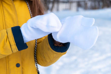 Young woman in yellow jacket putting on white mittens.の写真素材
