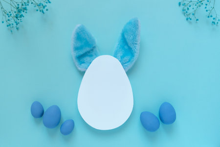 Easter composition with blue eggs and bunny ears placed under white egg shaped templateの写真素材