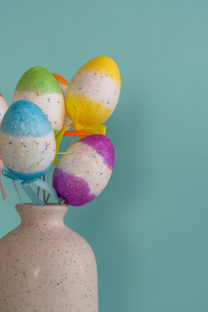 Bouquet of colorful Easter eggs placed in white vase against blue background