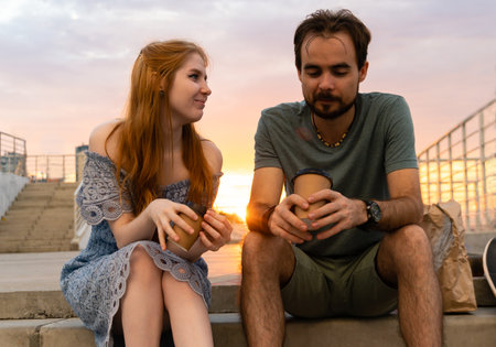 Young couple sitting on stairs with coffee in hands at sunsetの写真素材