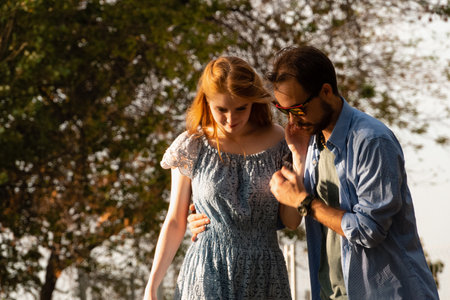 Young man helping girlfriend to ride longboard on sunny alley against green treesの写真素材