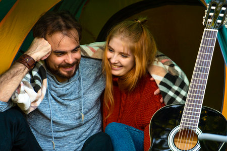 Laughing young couple sitting in camping tent hugging togetherの写真素材