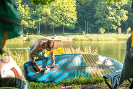 Young man preparing sup board for riding on shore of river