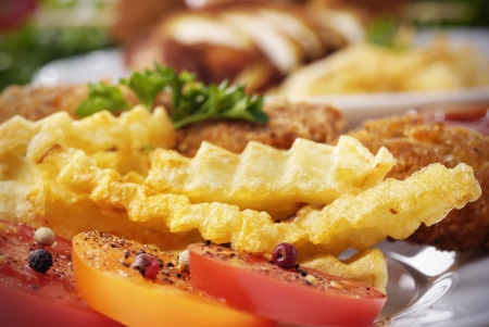 Fresh tasty french fries and chicken on the plate on the wooden table along with vegetables