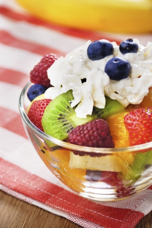 Sweet tasty fruit salad in the bowl with whipped cream on the wooden tableの写真素材