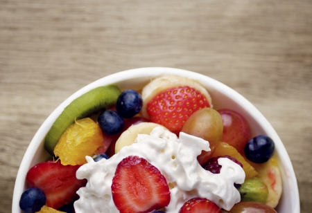 Sweet tasty fruit salad in the bowl with whipped cream on the wooden tableの写真素材