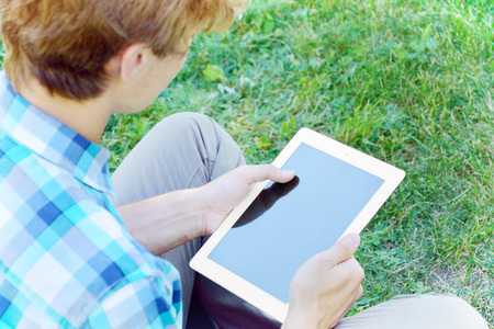 Young man is using tablet sittin on the grassの写真素材