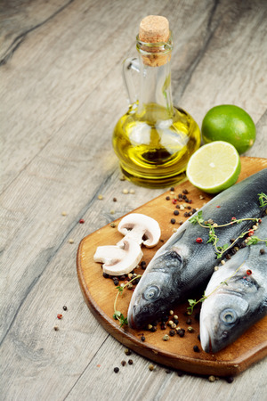 Raw seabass fish on the wooden board with vegetablesの写真素材