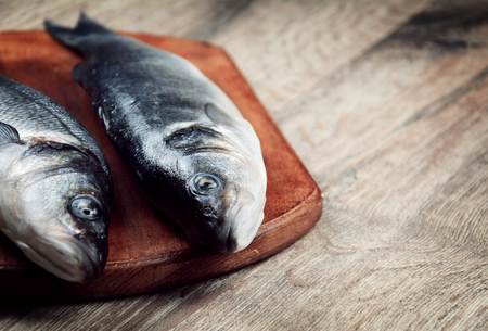 Raw seabass fish on the wooden board with vegetables