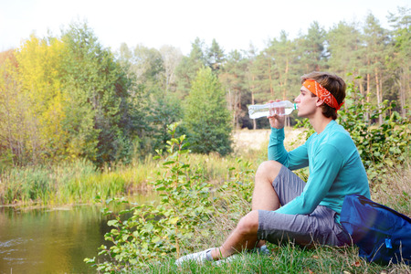 Young man is drinking water in the forestの写真素材