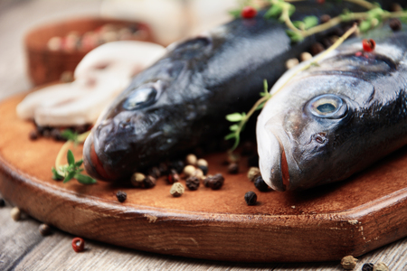 Raw seabass fish on the wooden board with vegetablesの写真素材