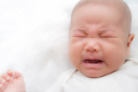Newborn Asian baby crying on bedの写真素材