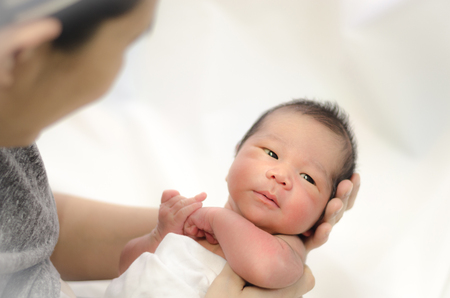 Asian Mother holding head of her newborn son in hands. The baby on hands at mom. Loving mother hand holding cute sleeping newborn baby childの写真素材