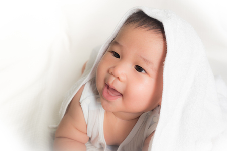 Portrait of excited male infant crawling and laughing on the bedroom under a white towelの写真素材