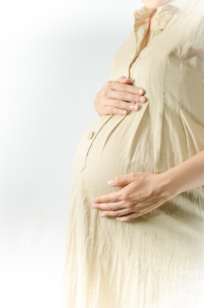 Close-up Image of pregnant woman touching her belly with hands on white backgroundの写真素材