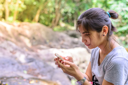Woman with mobile phone have rest on stone in forest.の写真素材