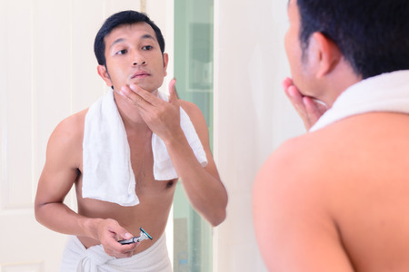 Young handsome man touching his smooth face after shaving with mirror.の写真素材