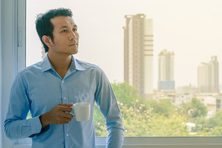 Businessman in shirt drinking hot coffee by window.
