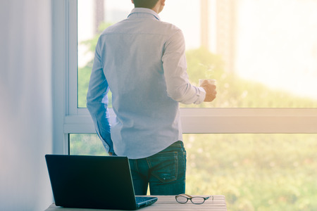 Businessman in shirt drinking hot coffee by window.の写真素材