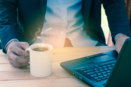 Businessman  holding coffee cup and typing a laptop on wooden table.の写真素材
