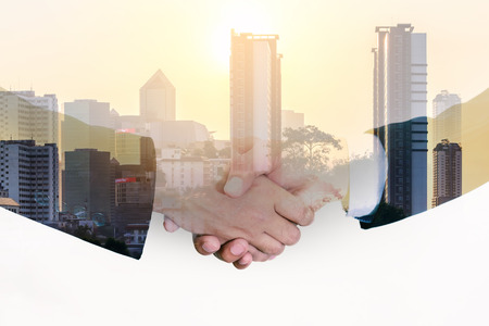 Double exposure closeup of businessmans handshake on city background.の写真素材