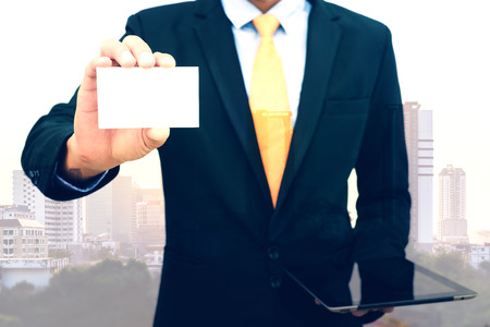 Double exposure of Businessman holding and showing blank business card on city background.の写真素材