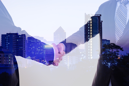 Double exposure closeup of businessmans handshake on city background.の写真素材