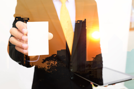 Double exposure of Businessman holding and showing blank business card on city background.の写真素材