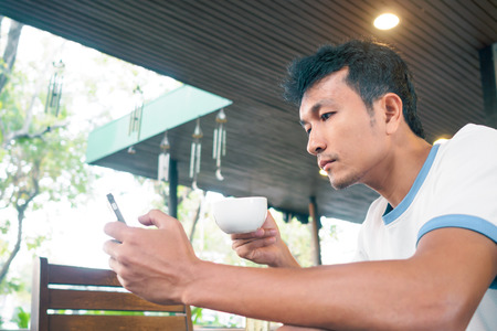 Handsome man use smartphone and drinking coffee.の写真素材