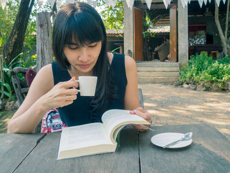 Asian woman relaxing with a coffee and reading a book.の写真素材