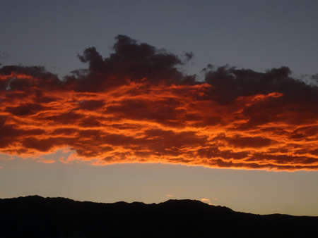 An vivid orange cloud band above a mountain range.                               
