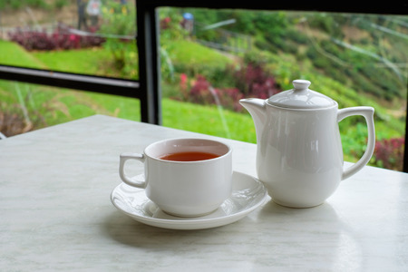 White cup of tea and teapot on white marble table in tea shop at Cameron Highlands, Malaysia.の写真素材