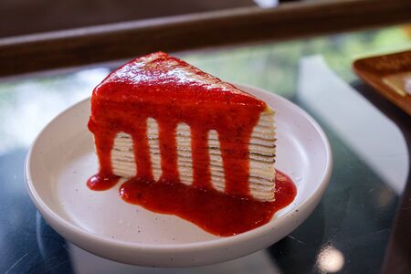 Crepe cake with strawberry sauce on a white plate in the coffee shop.