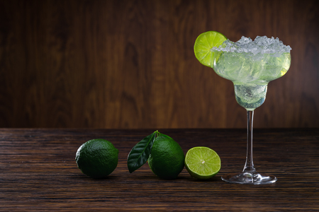 Glass of classical Margarita cocktail with ice and slice of lime on wooden table with fresh limes.の写真素材