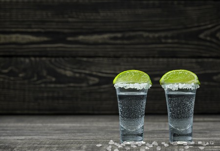 Two shot of Cold silver tequila with white salt crystals in lime on a black wooden backgroundの写真素材