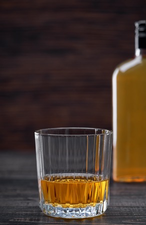 Black wooden table with highlight and a glass of hard liquor.の写真素材
