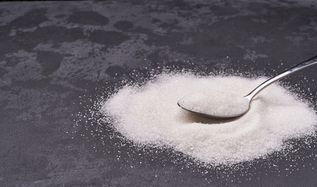 Close-up of granulated sugar in metal spoon and sugar pileの写真素材