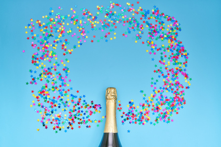 Creative photo of champagne bottle with colorful confetti on blue  background. Flat lay of christmas, anniversary, new year celebration conceptの写真素材