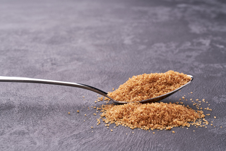 Close-up of granulated brown  sugar in metal spoon and sugar pile.Raw organic cane sugarの写真素材