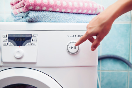 The washing machine which costs in a bathroom. The woman operates the washing machineの写真素材