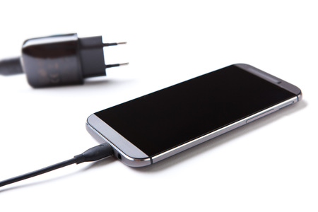 Mobile phone and charger are on the table.の写真素材