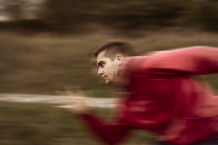 Young athlete with headphones running fast with motion blur effect added to photo. Phot shot from profile with shallow depth of fieldの写真素材