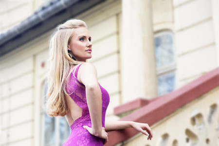 Portrait of young beautiful woman in formal pink dress that is posing on balcony looking aside the cameraの写真素材