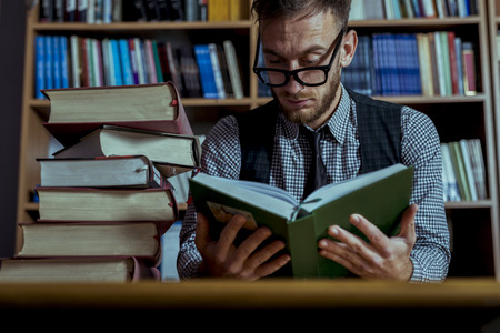 Student working hard over night in library going through books. Smartly dressed handsome man with...