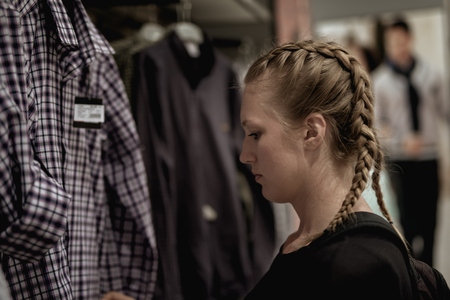 Beautiful Girl is shopping at the store. Looking at the shirt and checking the prices.