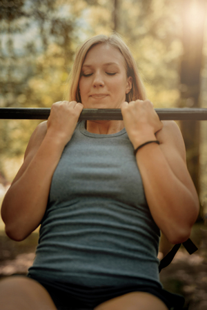 Young Beautiful Athletic Girl Exercising Outdoors at park. She is doing the pull ups with an effort.の写真素材